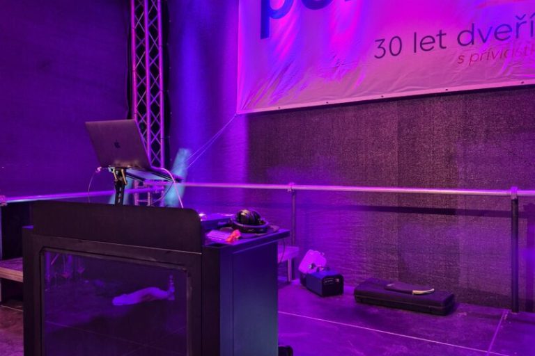 DJ pult a světelná rampa před bannerem k třicátému výročí firmy.